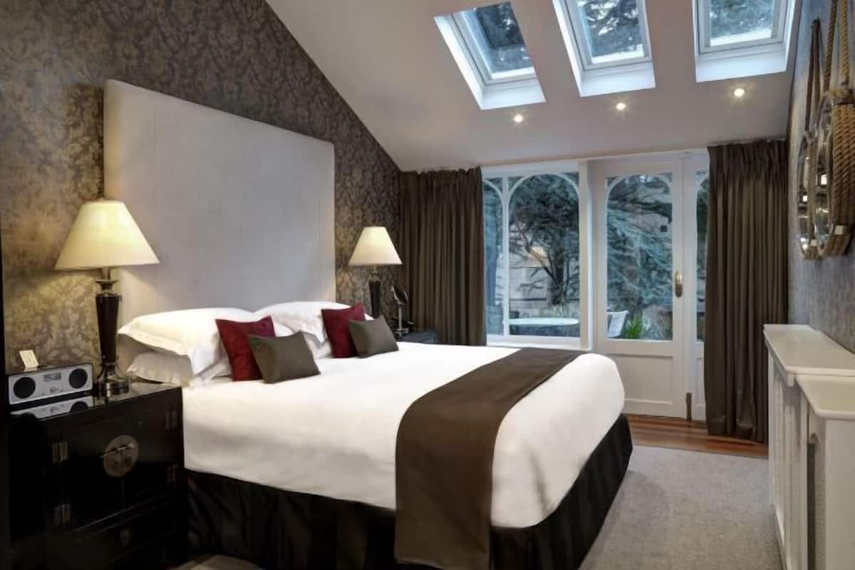 Une chambre d’hôtel avec un grand lit, deux lampes de chevet, une commode et une vue sur les arbres, visible à travers une porte vitrée.