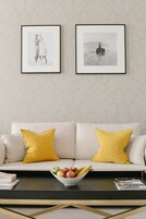 A living room with a white sofa, two yellow pillows, a coffee table with a bowl of fruit, and two framed pictures on the wall.