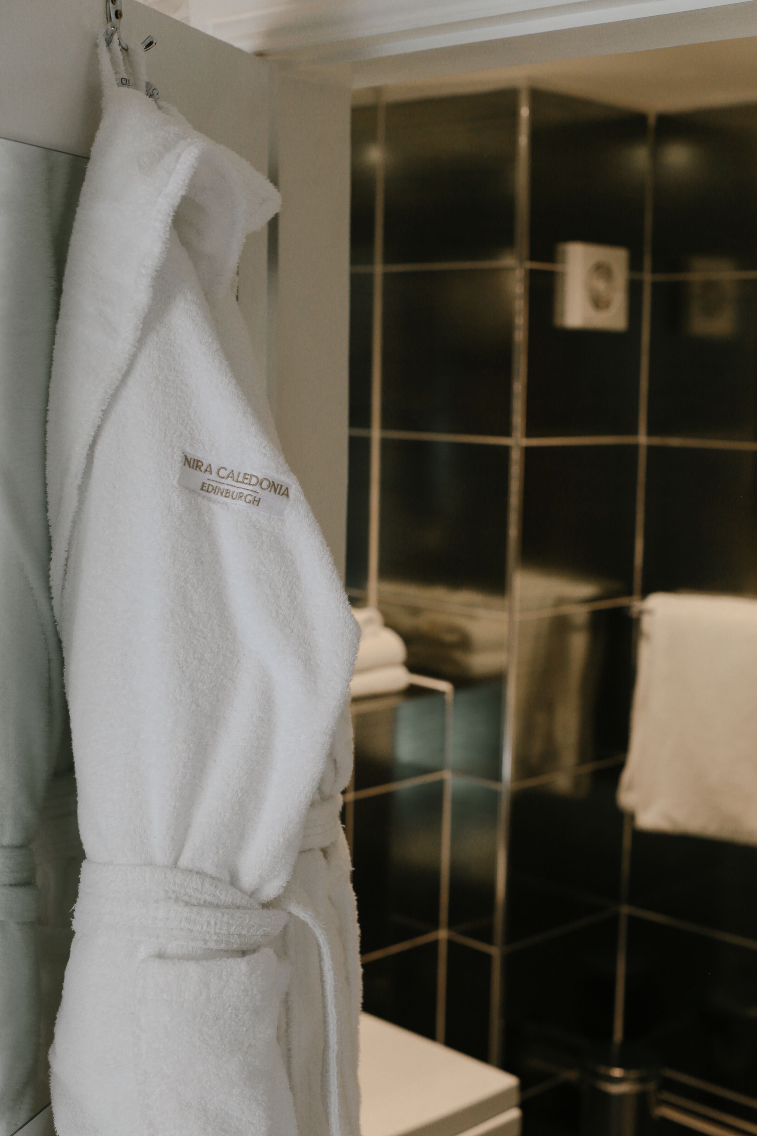 A white robe hanging on a hook in a bathroom with black tiled walls.