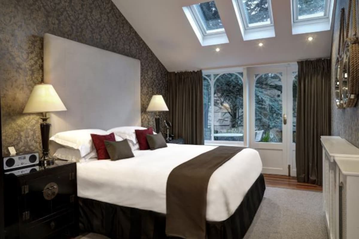 A hotel room with a large bed, two bedside lamps, a dresser, and a view of trees through a glass door.