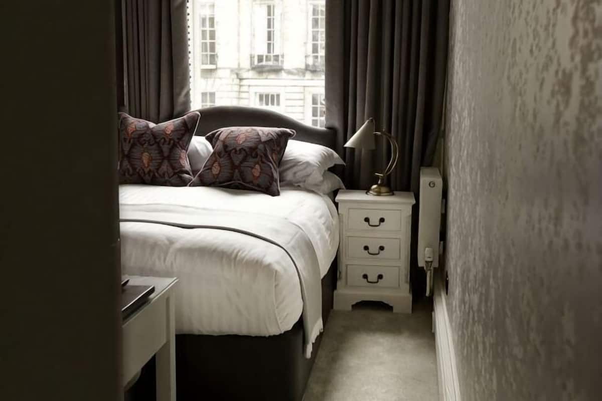 Une chambre à coucher avec un lit, des oreillers, une table de chevet, une lampe et une commode.