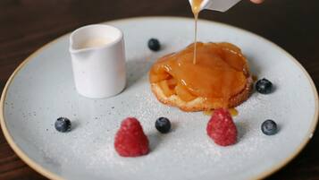 A dessert plate with a caramel apple, blueberries, and raspberries, and a small cup of cream.