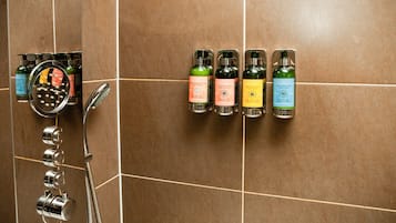 A shower area with a hand shower and a wall-mounted soap dispenser rack holding various bottles.