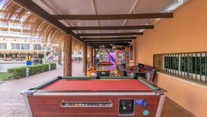 A pool table with a red felt surface, located in an outdoor area with a covered walkway and a building in the background. - Hotel Parasol by Dorobe (Torremolinos)
