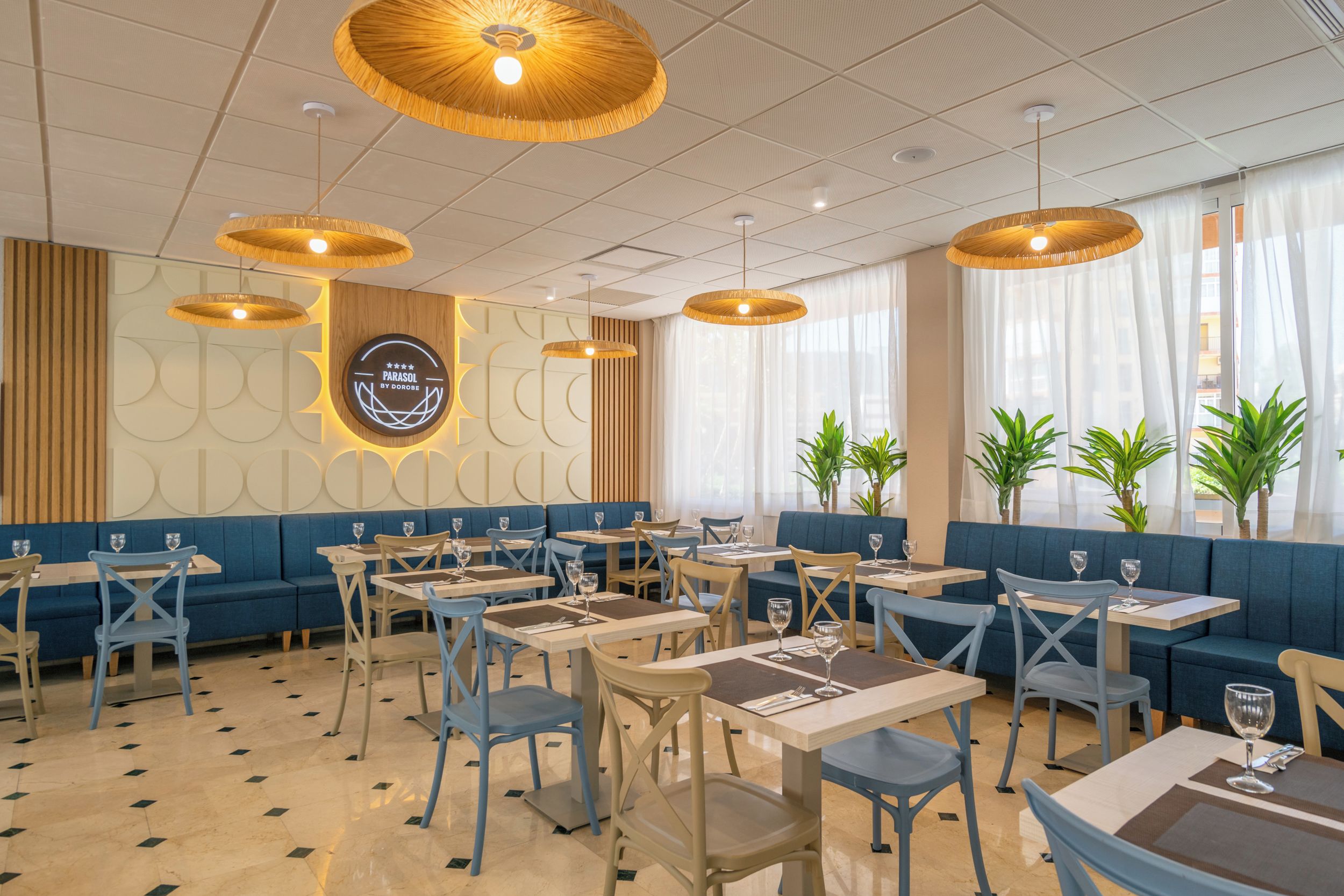 A restaurant interior with blue seating, wooden tables, and hanging wicker lamps.