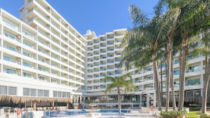 A multi-story hotel with a swimming pool surrounded by palm trees.