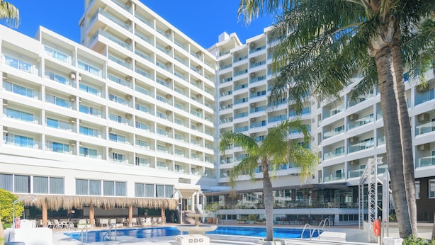 A hotel with multiple floors, a swimming pool, and palm trees.