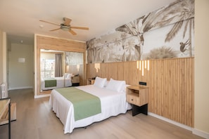 Hotelkamer met een groot bed, een plafondventilator, een houten wandpaneel en een muurschildering van tropische begroeiing.