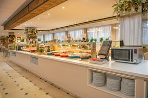 Een buffetruimte met diverse gerechten, een magnetron en een zithoek met stoelen.