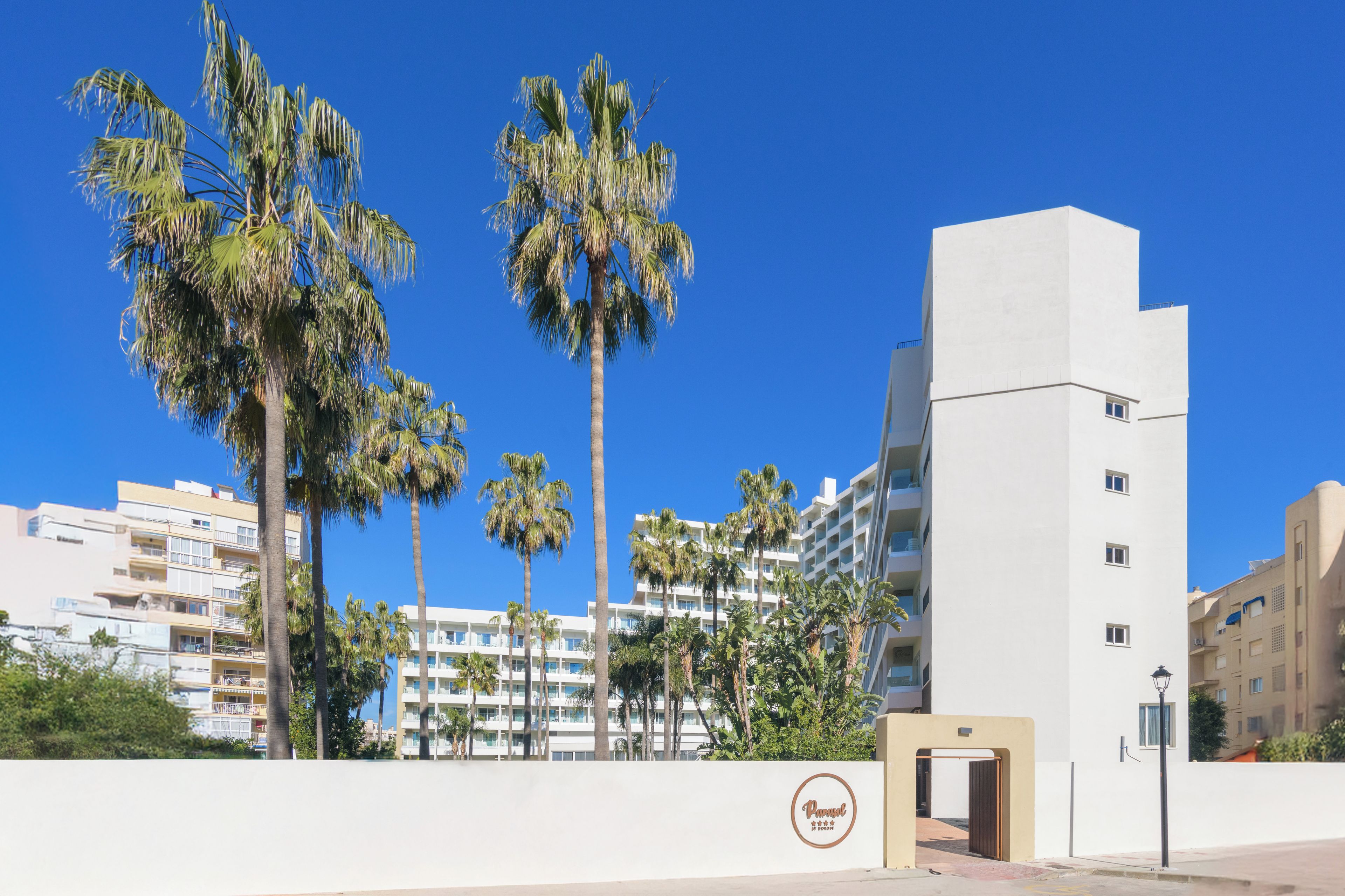 Un hotel de varios pisos, con palmeras y un cielo azul despejado.