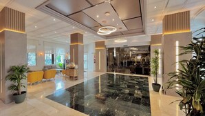 A spacious lobby with a marble floor, yellow chairs, and potted plants.