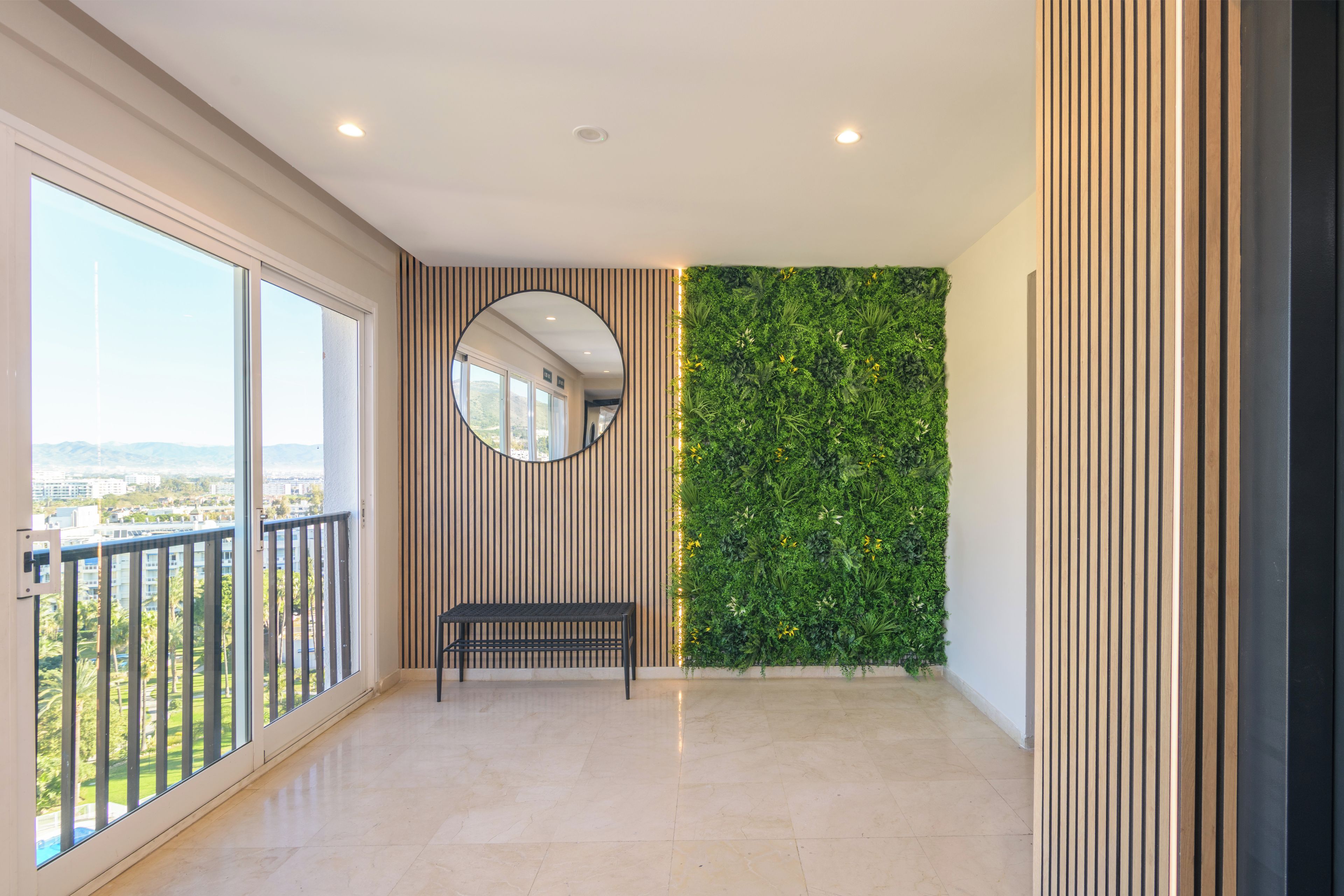 A spacious balcony with a view of the city, a round mirror, and a green vertical garden wall.