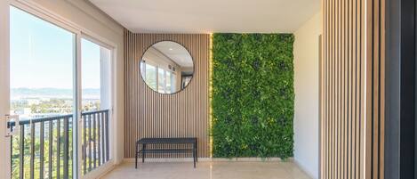 A spacious balcony with a view of the city, a round mirror, and a green vertical garden wall.