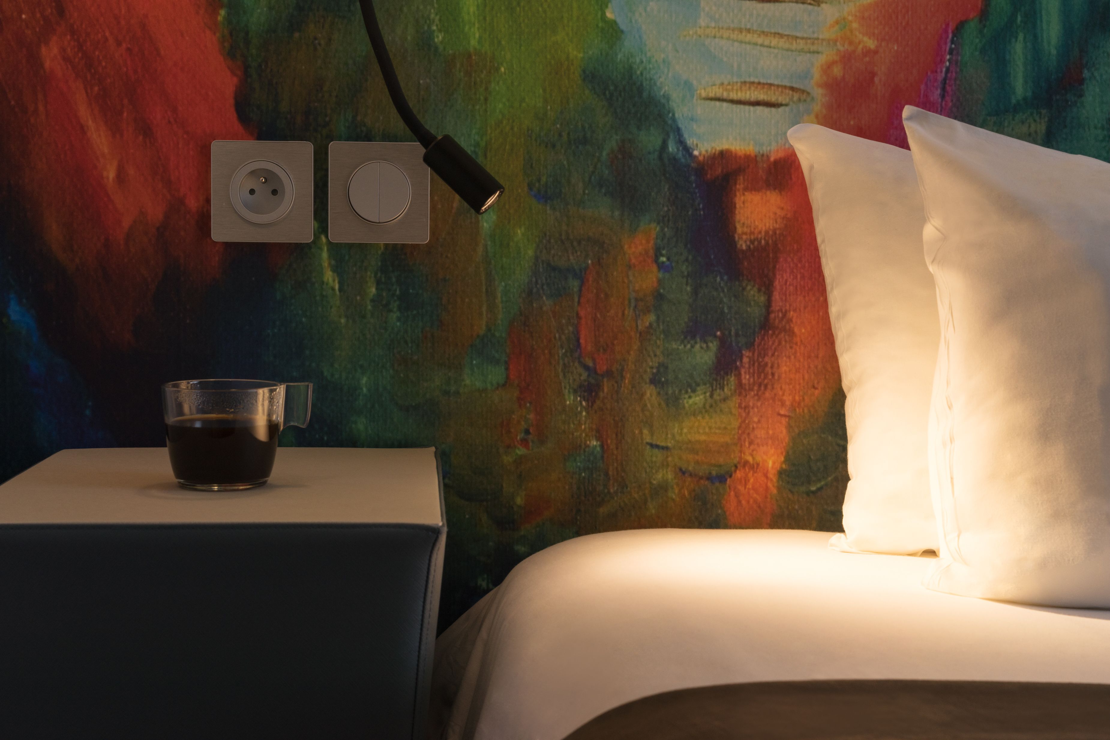 A bed with white pillows and a bedside table with a glass cup.