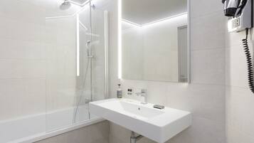 A modern bathroom with a white sink, a glass-enclosed shower, and a mirror with integrated lighting.