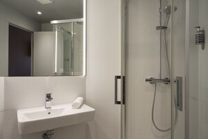 Un baño moderno con lavamanos blanco, cabina de ducha de vidrio y espejo.