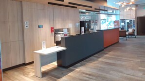 Un área de recepción moderna con un panel de madera, mostrador de recepción y una zona de estar con sillas.