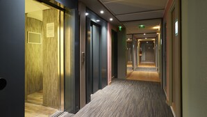 Un pasillo moderno de hotel con piso alfombrado, puertas de vidrio e iluminación empotrada.
