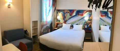 Habitación de hotel con cama, escritorio, silla, lámpara y un cuadro abstracto colorido en la pared.