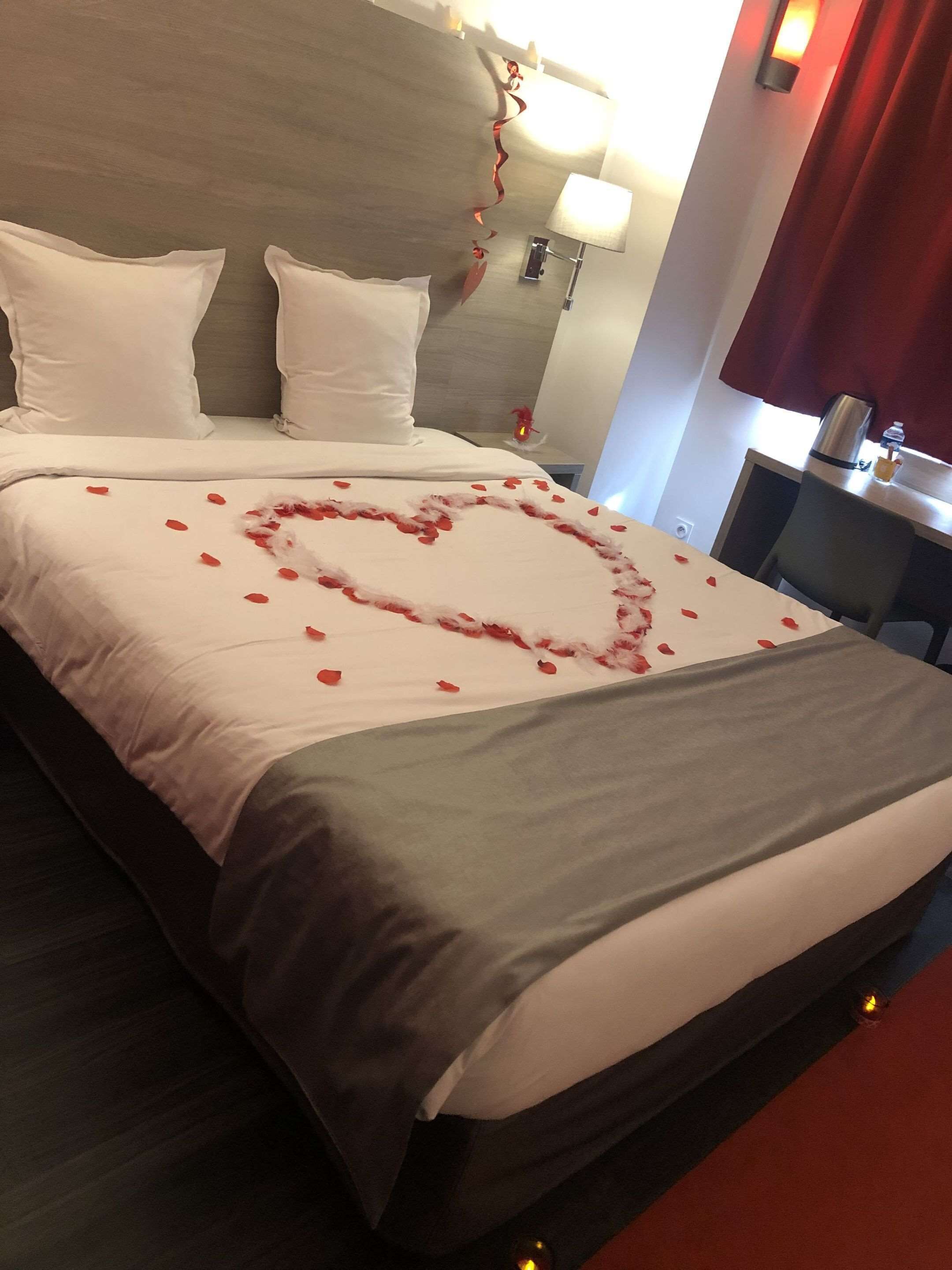 A hotel room with a neatly made bed, a headboard, a bedside table with a lamp, and a red curtain.