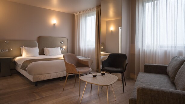 Una habitación de hotel moderna con una cama, dos sillas, una mesita y un sofá.