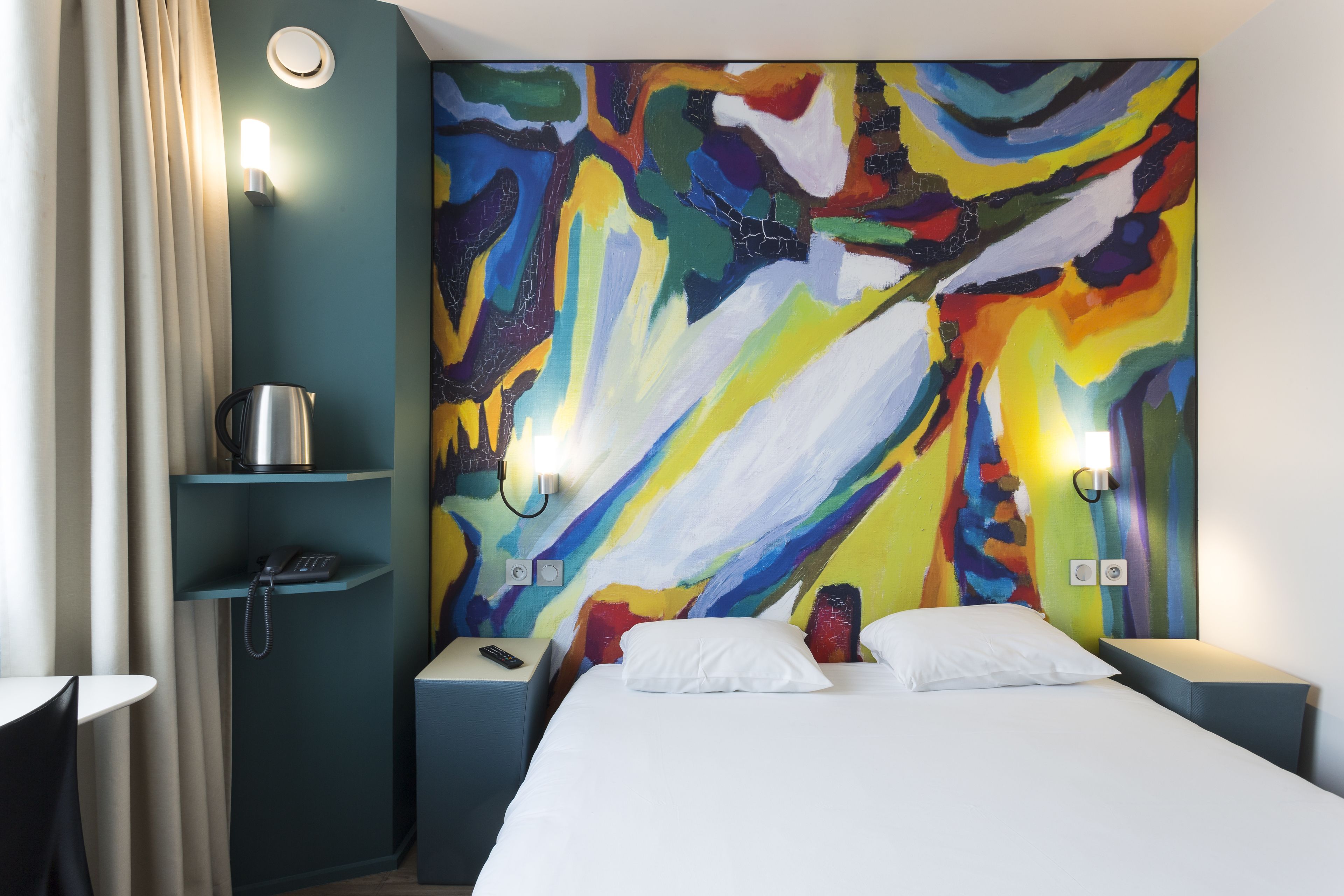 Ein Hotelzimmer mit einem großen, abstrakten Gemälde an der Wand, einem Bett mit weißen Bettwäsche, einem Nachttisch mit Lampe und einem Telefon auf dem Nachttisch.