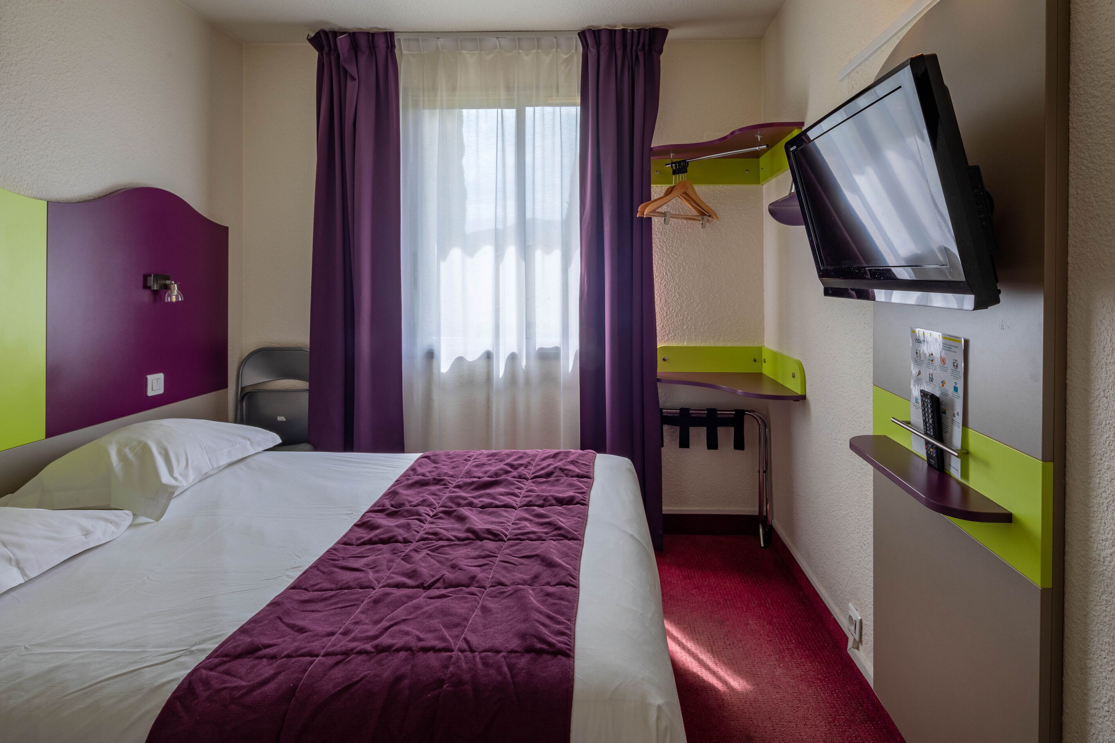 A hotel room with a bed, a desk, a television, and a shower.