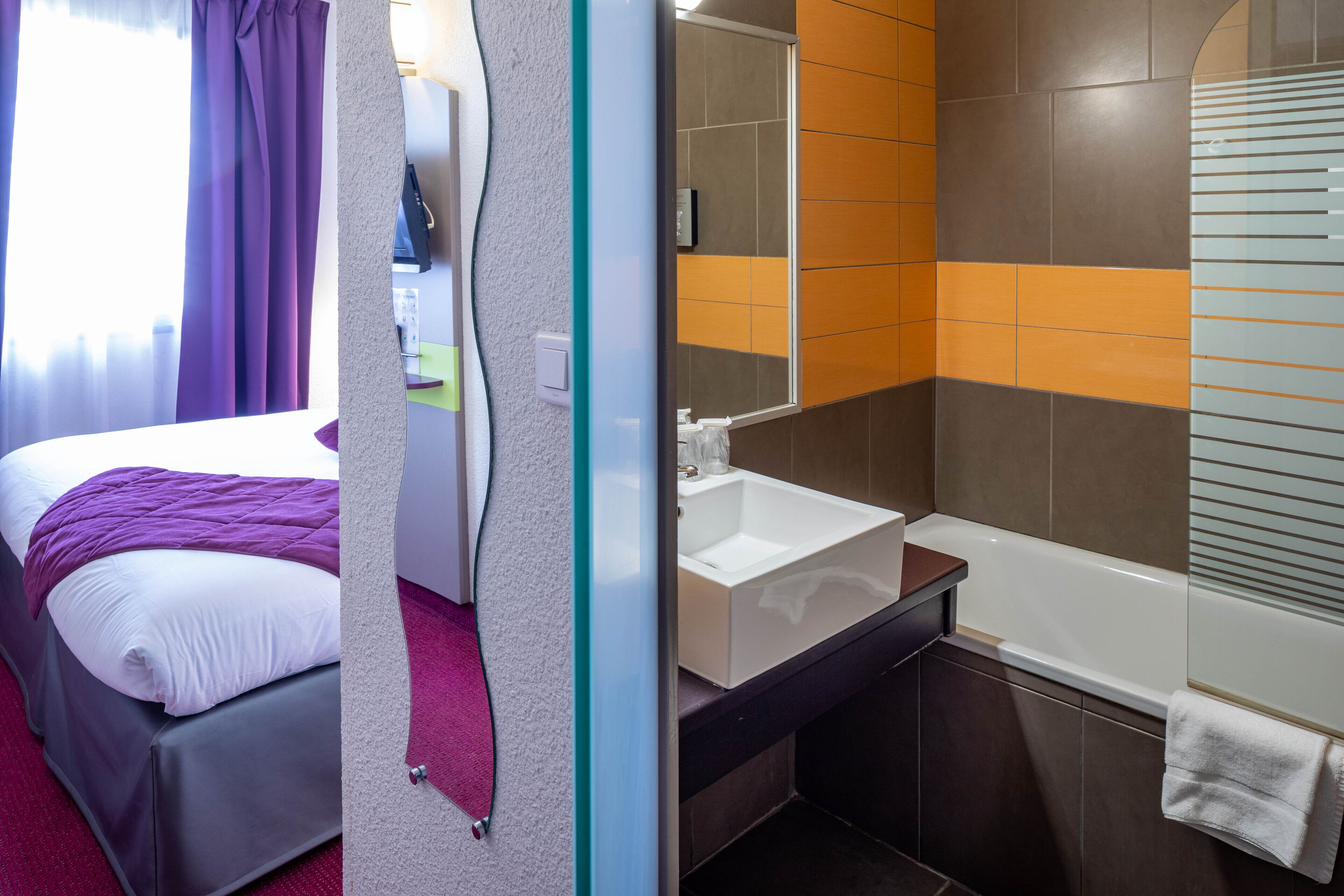 A hotel room with a bed, a bathroom with a bathtub, and a mirror.