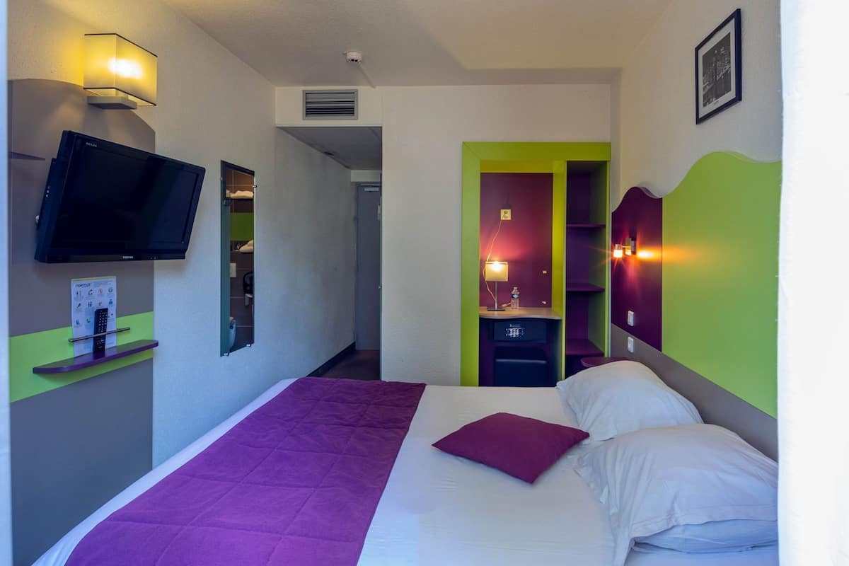 A hotel room with a bed, a television, a desk with a lamp, and a bathroom visible through an open door.