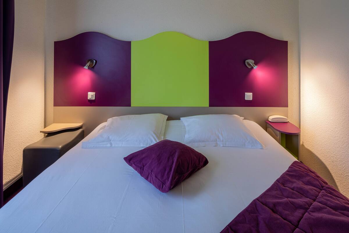 A hotel room with a bed, two bedside tables, and a headboard with a green panel.