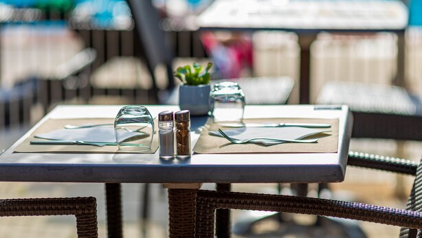 Una mesa de comedor con cubiertos, saleros y pimenteros, y una pequeña planta en maceta.