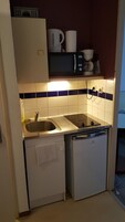 Uma cozinha compacta com pia, micro-ondas, cafeteira e geladeira compacta.