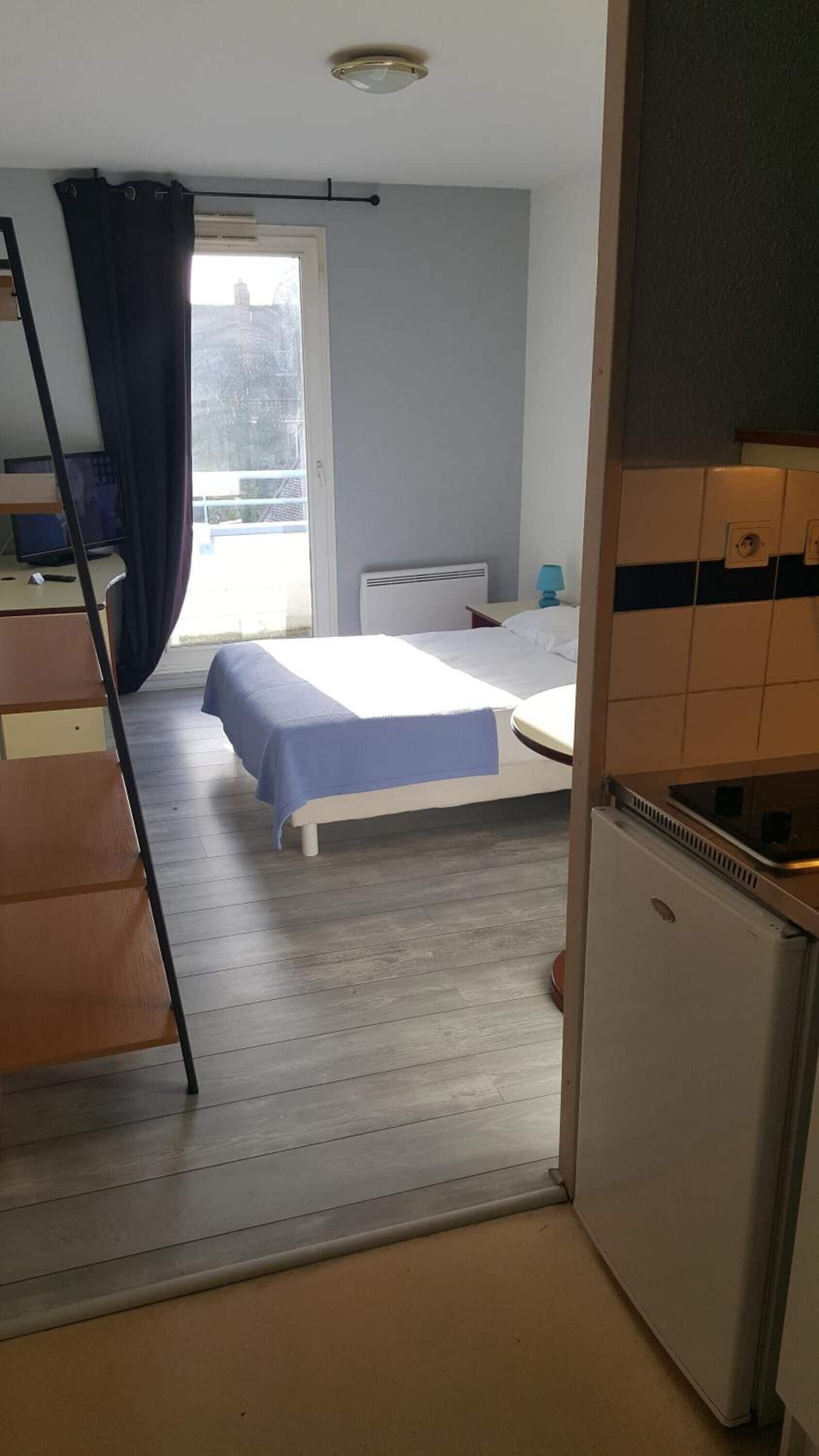 A small, compact room with a bed, a desk, and a kitchenette.