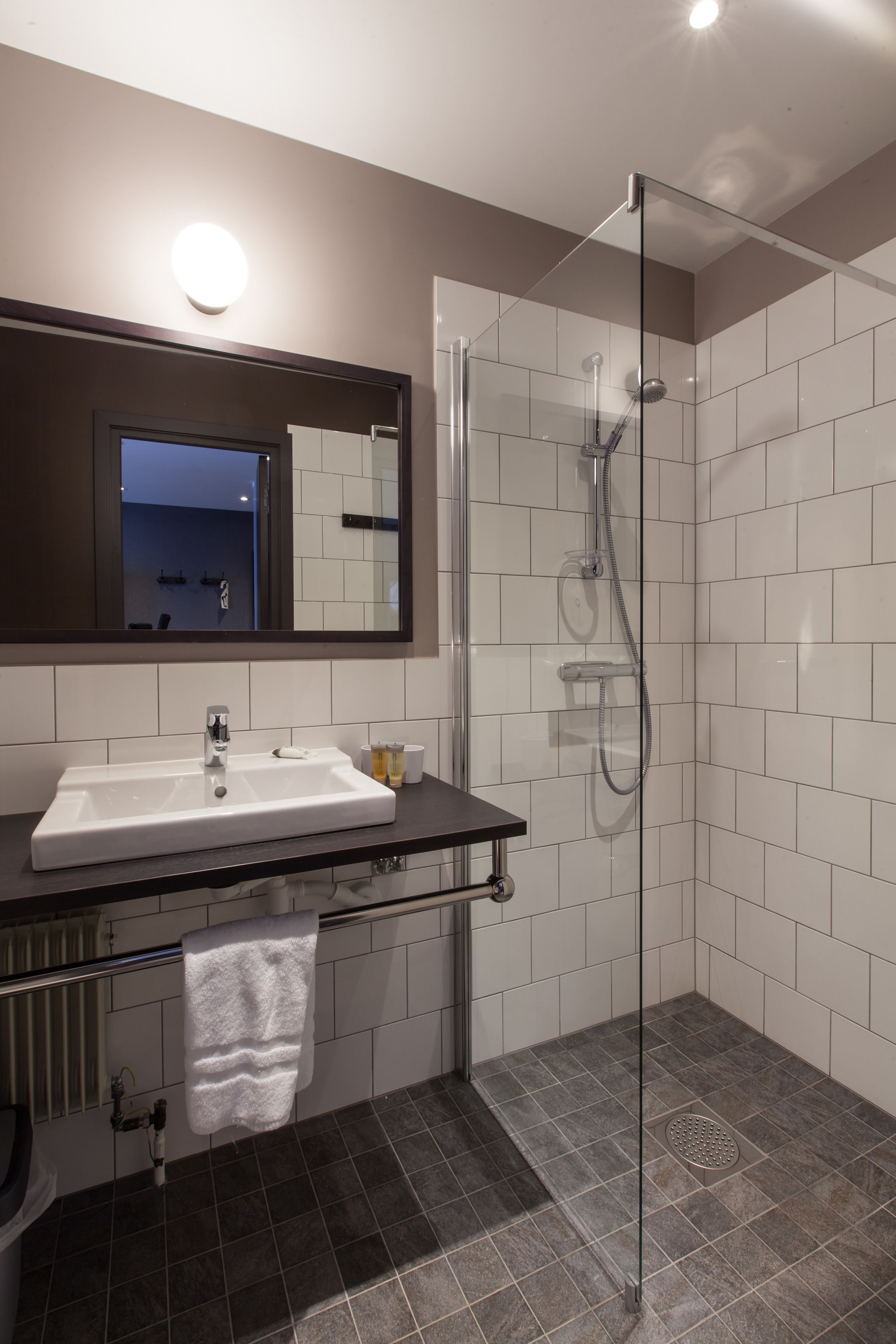A modern bathroom with a glass-enclosed shower, a large mirror, and a dark countertop.