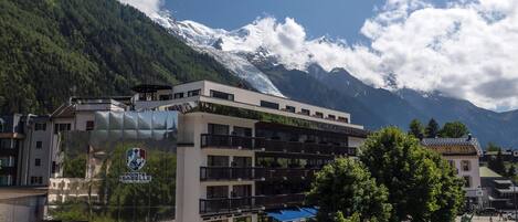 A hotel with a modern design, featuring balconies and a view of snow-capped mountains.