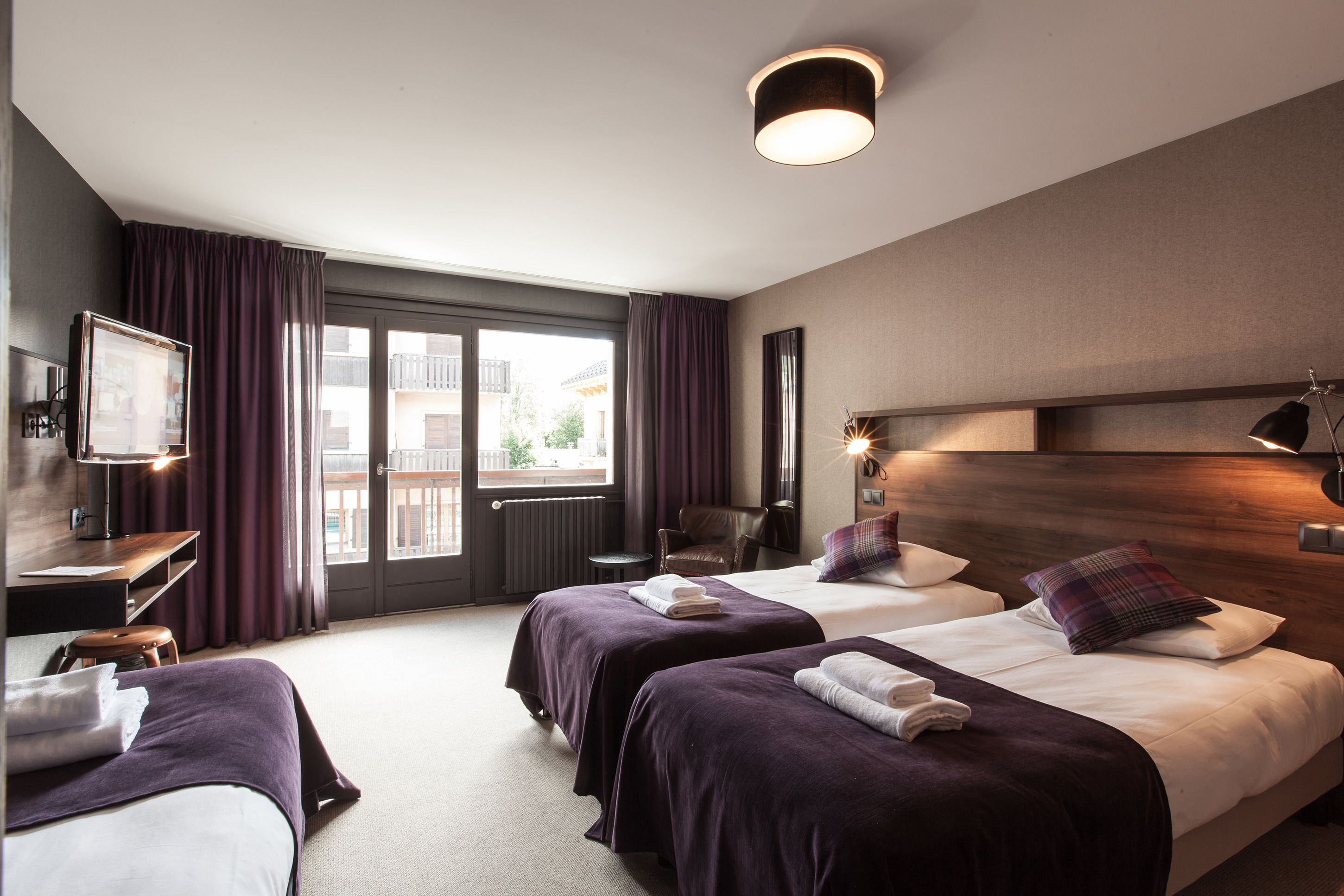A hotel room with two beds, a desk, a chair, and a view of the outside.