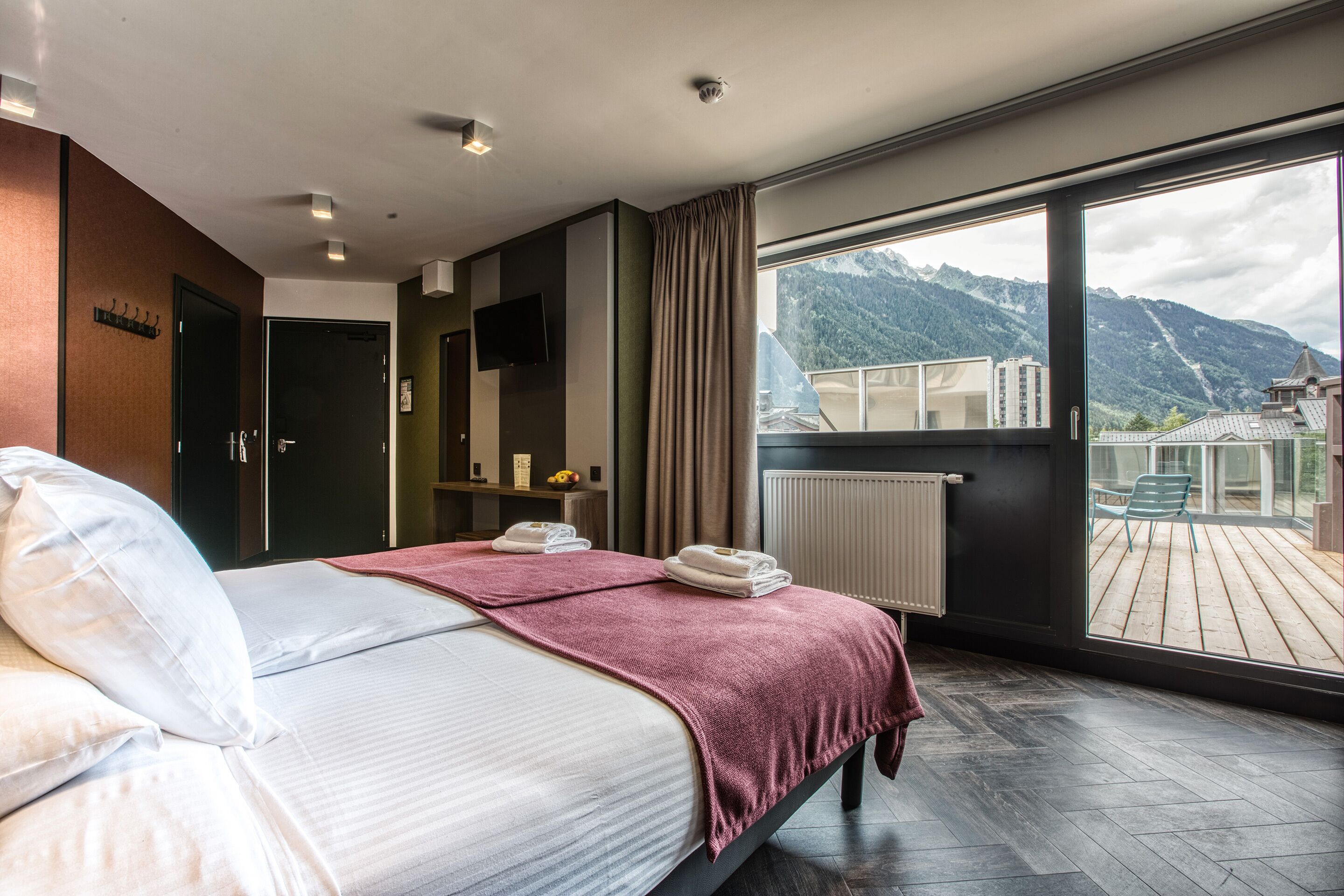 A modern hotel room with a large bed, a view of mountains, and a balcony with outdoor furniture.