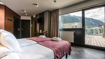 A modern hotel room with a large bed, a view of mountains, and a balcony with outdoor furniture.