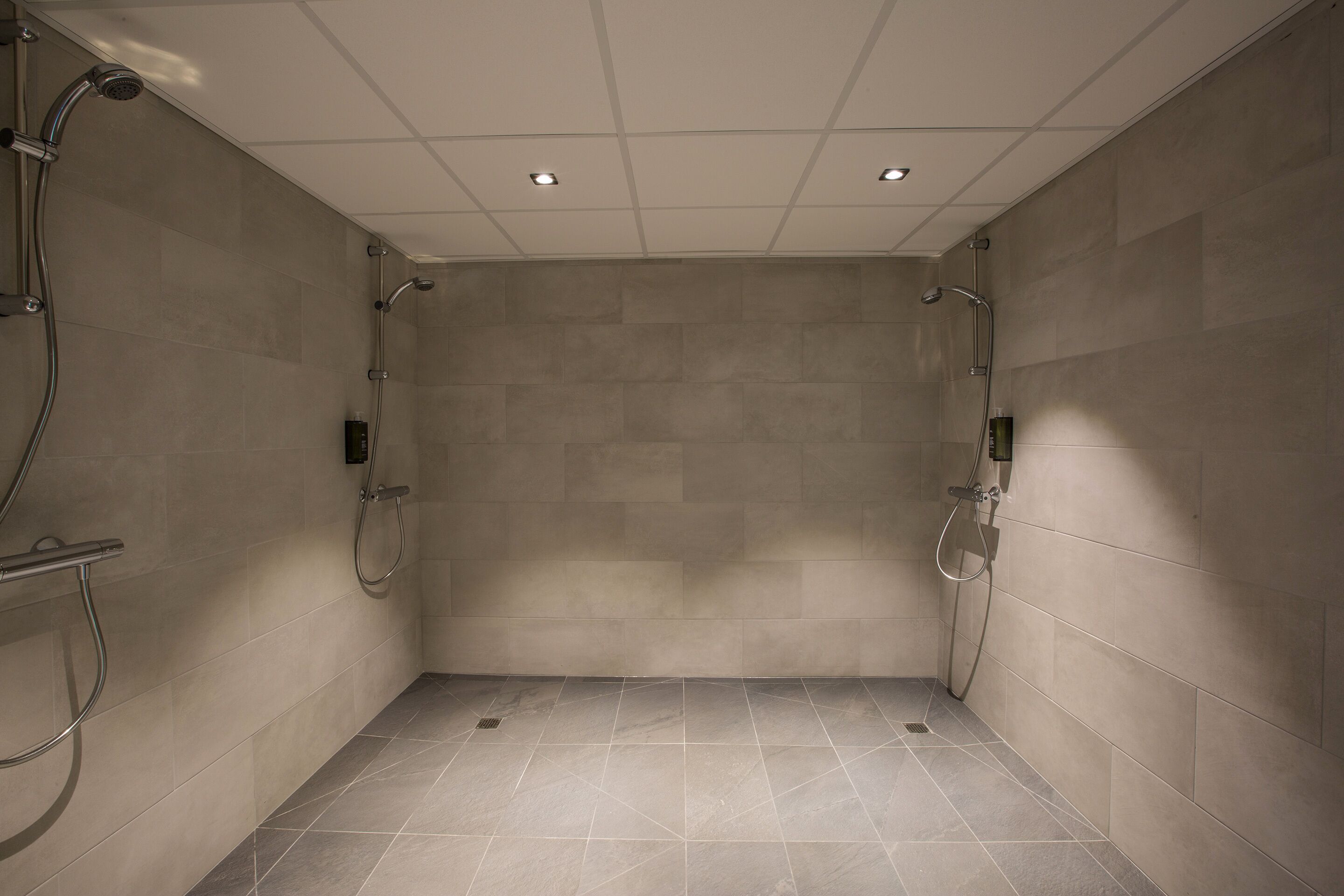 Une salle de douche moderne avec des murs et un sol carrelés, équipée d’un pommeau de douche à main et d’un pommeau de douche fixe.