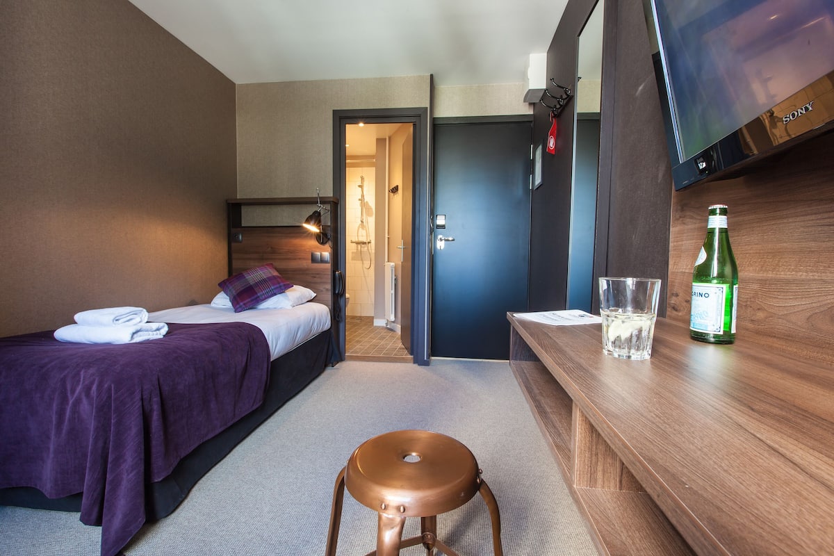 Ett hotellrum med en säng, en pall, en tv och en flaska vatten på bordet.