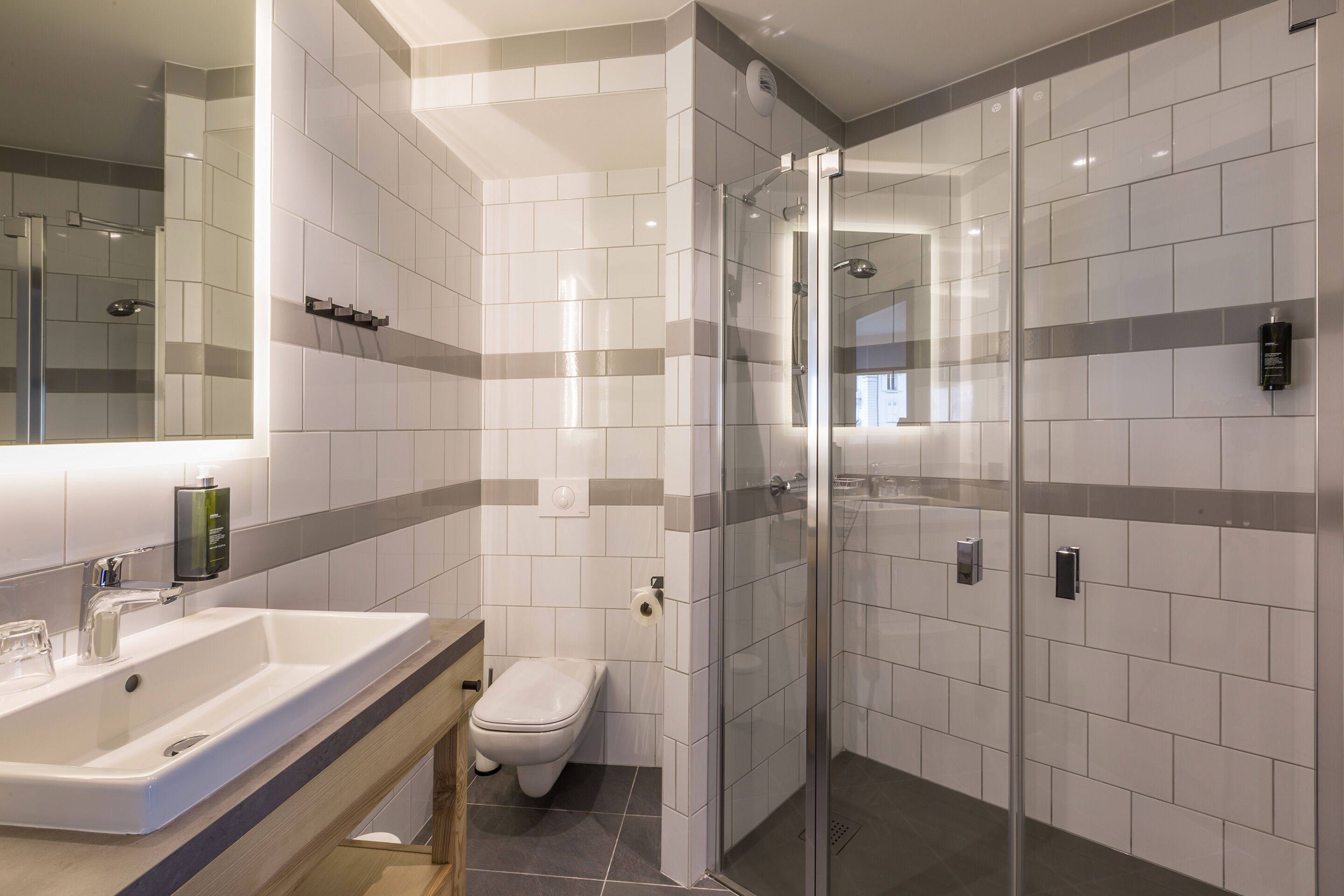 Et moderne badeværelse med et stort spejl, en vask, toilet og en bruseafskærmning af glas.