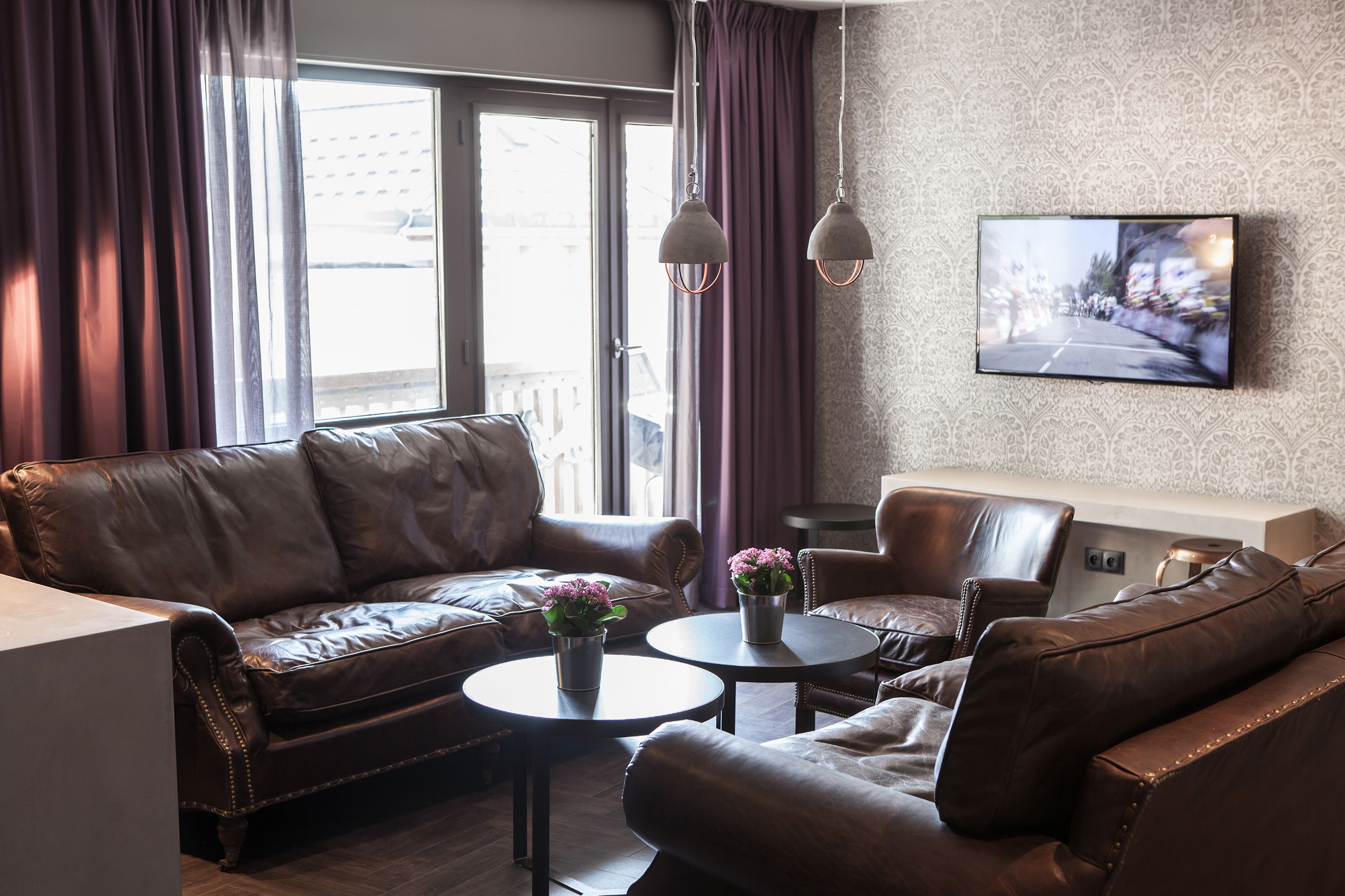 A modern living room with a leather sofa, two round tables, and a TV mounted on the wall.