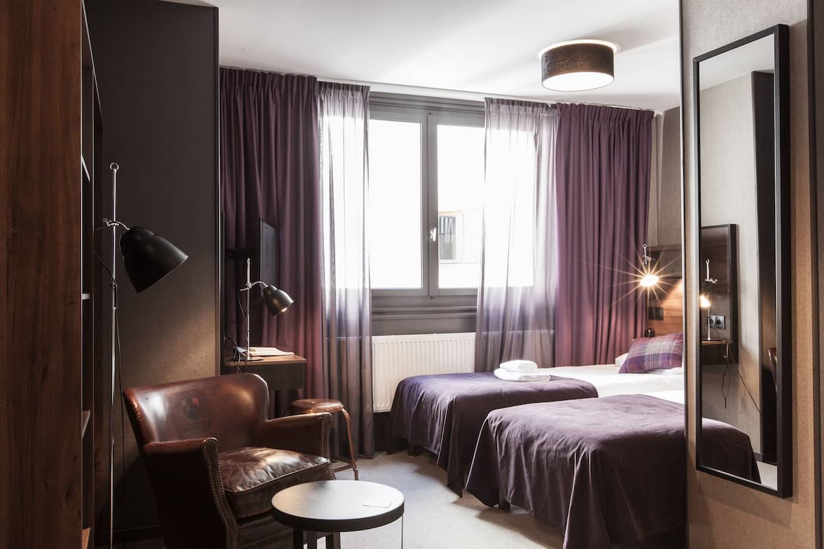 Ett hotellrum med två sängar, ett skrivbord, en stol, en lampa och en stor spegel.