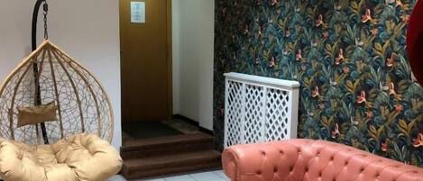 Un salón con un sofá de cuero capitonado, un sillón colgante, un papel tapiz estampado y una escalera que lleva a otra habitación.