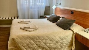 Una cama bien hecha con un cubrecolcha acolchado, una lámpara de noche y una mesita de noche de madera con un teléfono.