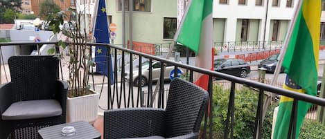 Ein Balkon mit Korbmöbeln, Blick auf ein Hotel und Flaggen verschiedener Länder.