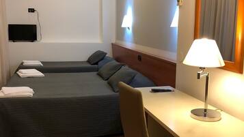 Ett hotellrum med två sängar, ett skrivbord, en stol, en tv och en lampa.