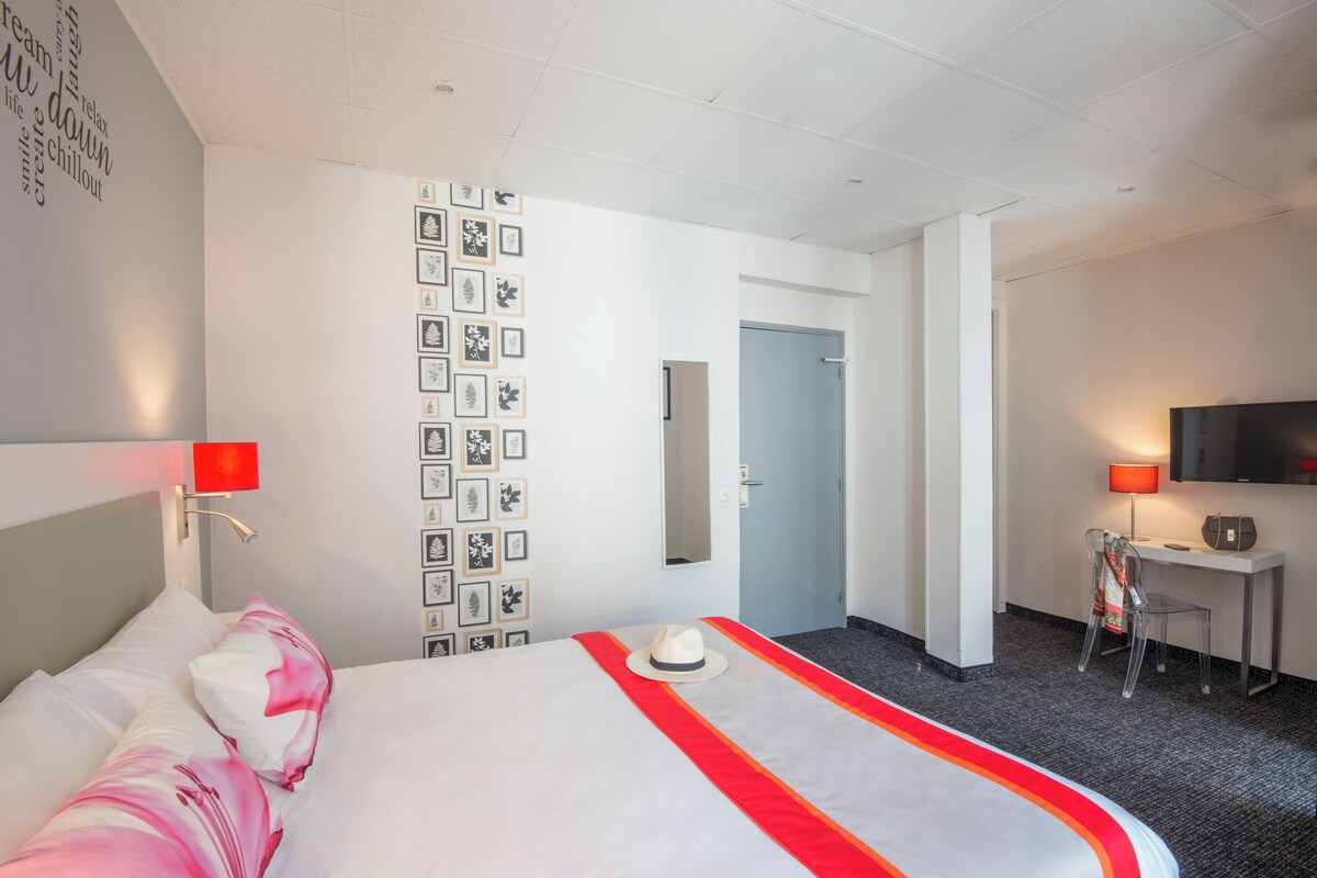 Ein Hotelzimmer mit einem Bett, einem Schreibtisch, einem Sessel, einem Fernseher und einer Wand mit gerahmten Bildern.