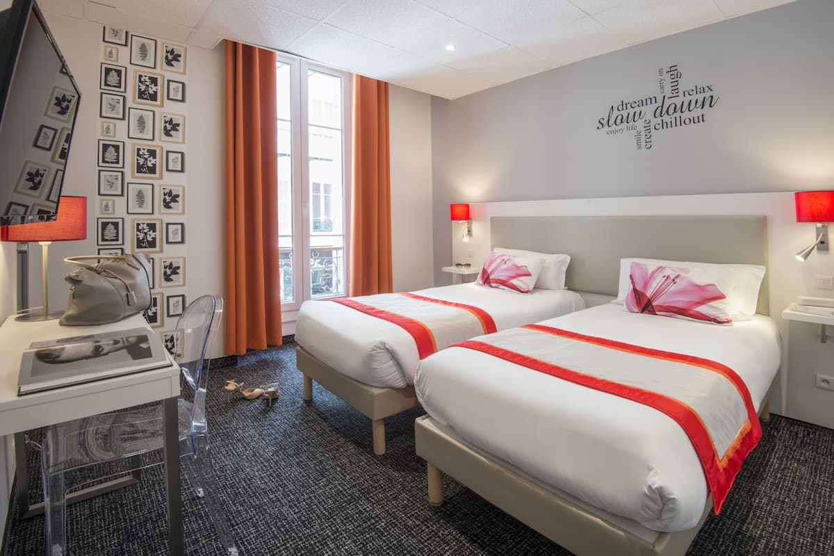 Ein Hotelzimmer mit zwei Betten, einem Schreibtisch mit einem Laptop, einem Stuhl und einem Fenster mit Vorhängen.