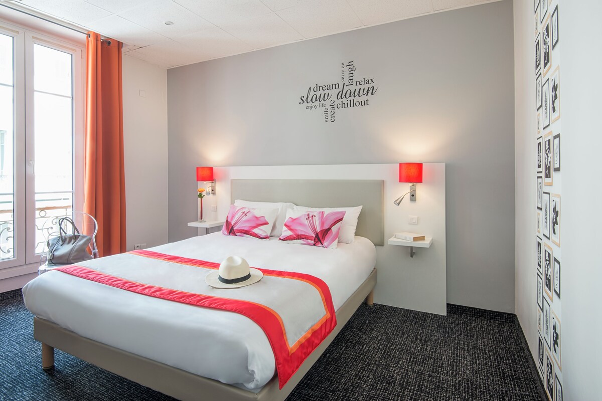 Habitación de hotel con una cama grande, dos lámparas de noche, una pared con mensajes motivacionales y vistas al exterior.